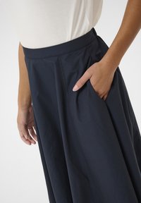 Gonna blu navy, lunghezza al ginocchio, realizzata in tessuto liscio con una vita aderente e una tasca laterale, caratterizzata da delicate pieghe per un volume extra.