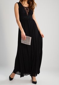 Lång svart klänning med en spetsöverdel, svävande kjol och bälte i midjan. Kombinerad med en metallisk kuvertväska och svarta skor.