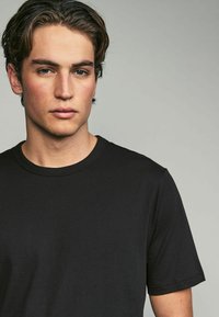 Camiseta de algodón negra con mangas cortas, cuello redondo y una textura suave. Diseño sencillo sin patrones o acentos visibles.