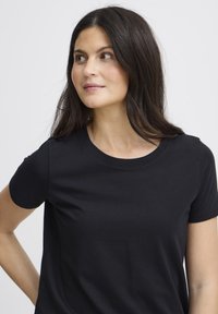 Fekete rövid ujjú póló kerek nyakkivágással. Puha pamut anyagból készült, sima textúrával és testhez álló szabással.