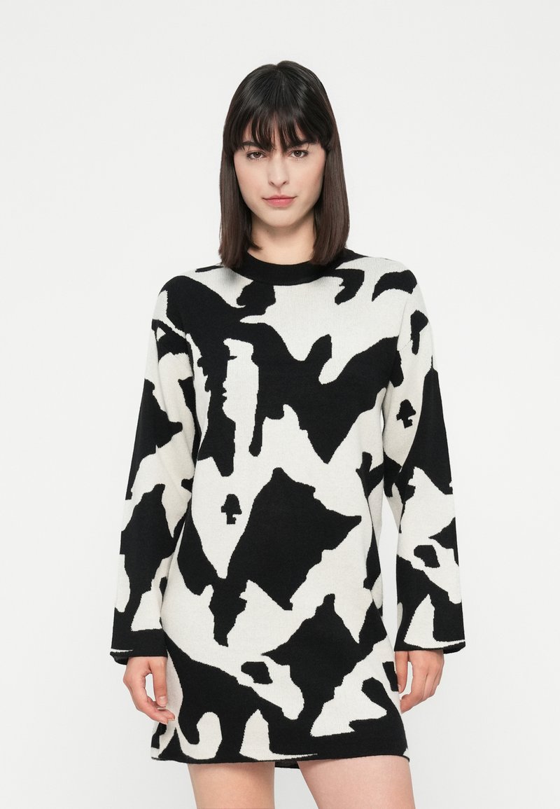 Zwart-wit gestreepte oversized trui-jurk met lange mouwen, ronde hals en abstracte vormen door de stof.