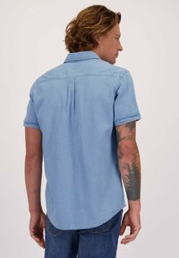 Lichtblauw denim overhemd met korte mouwen, een brede kraag, een plooitje aan de achterkant en een afgeronde zoom. Heeft zichtbare stiksels en een gestructureerde stof.