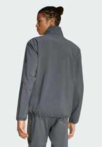 Šedá ľahká bunda s vysokým golierom, elastickými manžetami a voľným strihom. Hladká textura a minimálny dizajn, s rovnými chrbtom.