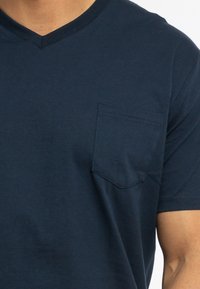 Marineblaues Baumwoll-T-Shirt mit V-Ausschnitt und kleiner Brusttasche links. Glatte Textur und kurze Ärmel, geeignet für Freizeitkleidung.