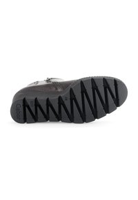 Black rubber boot sole with pronounced treads, featuring zigzag patterns for traction. Smooth upper section with zipper detail along the side.