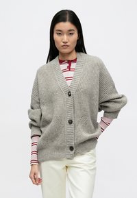 Hall hallatud kardigan V-kaelusega, soonikservadega ja kolme suure nööbiga. Omab suurendatud varrukaid ja kahte esitaskut.