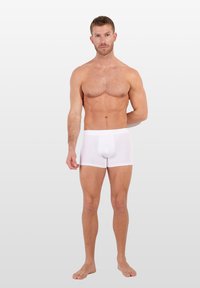 Bílé bavlněné boxerky s přiléhavým střihem, elastickým pasem a hladkou texturou, vystavené na mužském modelu stojícím naboso.