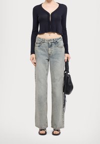 Granatowy kardigan z prążkowanej tkaniny, krótki, z zamkiem błyskawicznym z przodu, zestawiony z jasnoniebieskimi spodniami typu wide-leg. Dodatki to czarna torba i sandały.