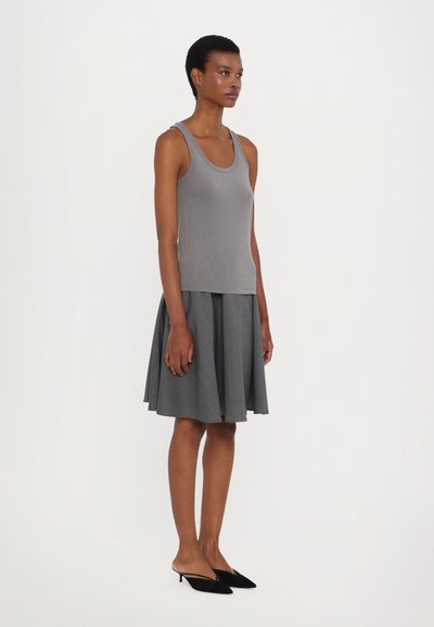 Gray tank top paired with a flared gray skirt, featuring a smooth texture. Model wears black heeled mules. Simple, minimal design.