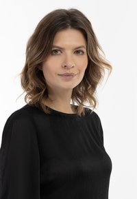 Top negru dintr-o țesătură netedă și texturată; prezintă un decolteu rotund și o siluetă lejeră. Păr ondulat și de lungime medie, până la umeri.