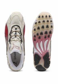 Sneakers med en cremefarvet overdel, røde og sorte accenter, struktureret gummisål med flere stød og justerbare snørebånd. Puma-logo synligt.