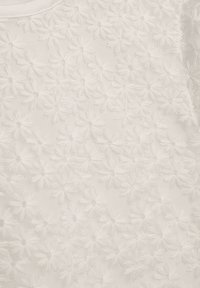Weißer Stoff mit gestickten Blumenmustern, deren strukturierte Blütenblätter eine erhabene Wirkung auf der Oberfläche erzeugen.