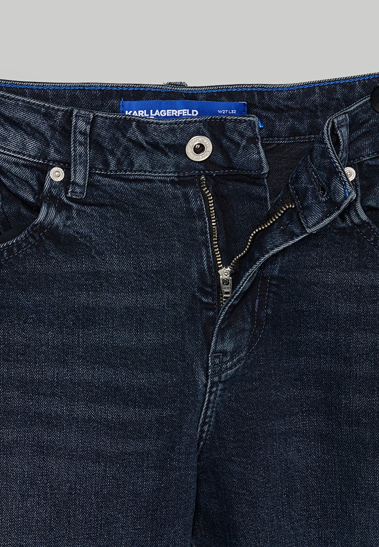 Dunkelblaue Jeans mit mittelhohem Bund, ausgestattet mit einem silbernen Metallreißverschluss, Knopfverschluss und Jeansstruktur. Das Etikett zeigt die Größe W27 L32.