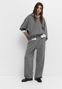 Hanorac oversized gri cu buzunar frontal, asortat cu pantaloni sweat de tip wide-leg. Material gros cu mansete ribbate și o croială relaxată.