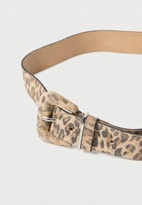 Lauvas raksta ādas josta ar gludu beigh krāsas apakšpusi, kurai ir sudraba metāla sprādze un siksna ar vairākiem pielāgošanas caurumiem.