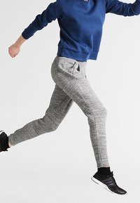 Grå atletiska joggers med en texturerad yta och elastisk midja, kombinerat med en blå sweatshirt och svarta atletiska skor.