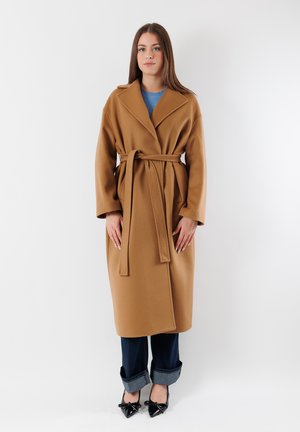 Soprabito in misto lana marrone con vita con cintura, colletto a scollo e maniche ampie. Abbinato a jeans scuri con risvolto e tacchi neri a punta.