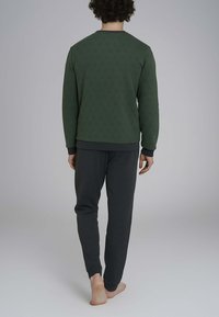 Felpa verde a fantasia con accenti rossi e pantaloni grigio scuro. La felpa presenta un colletto e dei polsini a coste. A piedi nudi.