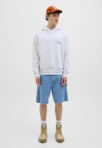 Grå bomulds hoodie med kængurulomme, blå denim shorts, beige snørebåndsstøvler og en brun kasket med et hvidt logo.