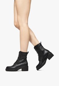Bottines noires en cuir lisse, avec un laçage à l'avant, une fermeture éclair et un talon chunky texturé.