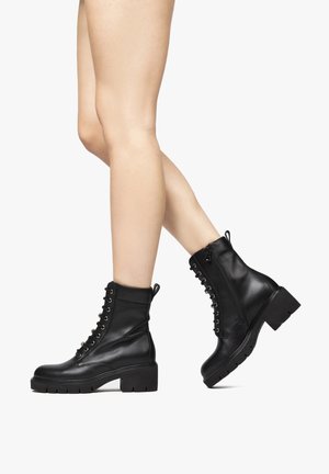 Black ankle boots made of smooth leather, featuring a lace-up front, zipper closure, and a chunky, textured heel.