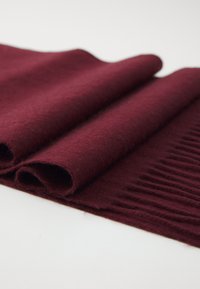 Folded soft burgundy wool scarf with ribbed texture on one end, laid on a white surface.