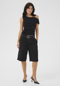 Black, off-shoulder top with ruched texture paired with tailored black shorts and a matching belt, complemented by pointed black heels.
