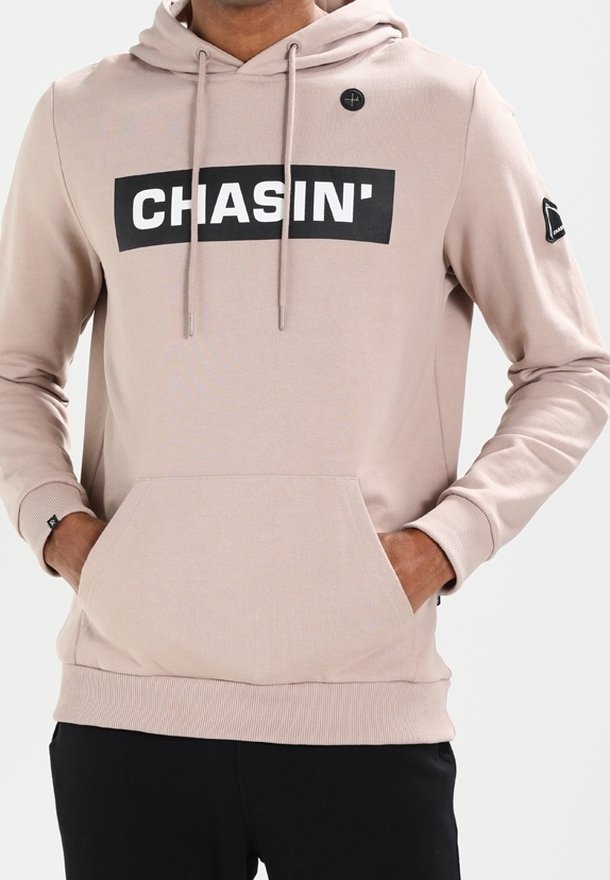Felpa leggera beige chiaro con logo nero "CHASIN'" sul petto, coulisse regolabile, tasca anteriore e dettagli neri sulle maniche.
