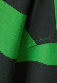 Zwart en groen gestreepte stof met een zachte textuur. De groene strepen zijn levendig en contrasteren met de donkere zwarte delen. Zichtbare stiksels.