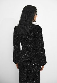 Rochie neagră din mărgele cu mâneci lungi, stofă texturată, siluetă ajustată și finisaj neted, care prezintă o suprafață strălucitoare.
