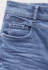 Ljusblå denimtyg med en slät yta, med en liten framficka och synliga söm detaljer längs midjan och kanterna.