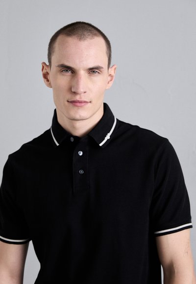 Black polo shirt made of cotton, featuring a two-button placket and white striped accents on the collar and sleeves. Smooth texture.