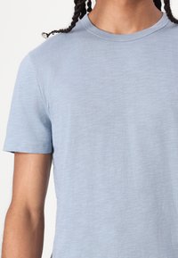 Camiseta de crewneck azul claro, hecha de un tejido suave, con mangas cortas y una textura sutil. Sin patrones ni acentos visibles.