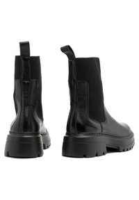 Czarne skórzane botki za kostkę z prążkowanymi panelami bocznymi, teksturowanym wykończeniem i masywnymi gumowymi podeszwami. Z tyłu znajdują się pętle ułatwiające zakładanie.