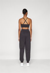 Reggiseno sportivo nero con spalline incrociate, abbinato a pantaloni deliziosamente larghi neri e sneakers bianche, visto da dietro.