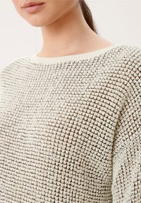 Sweter dzianinowy w kremowym kolorze z teksturowanym, otwartym splotem; posiada szeroki dekolt i ściągacze przy mankietach dla swobodnego kroju.