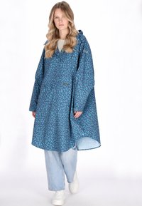 Kék leopárdmintás kabát kapucnival, bő szabással és hosszú ujjakkal. Az anyag simának tűnik, a lábszár közepéig ér, világoskék farmerral párosítva.