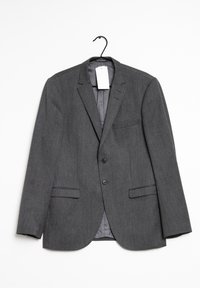 Grå blazer hängande på en krok. Har en skarp krage, två framfickor och en enda bröstficka. Tyget har en subtil struktur.