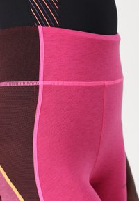 High-waisted workout leggings in pink and brown. Features contrasting color panels, textured fabric, and flatlock stitching.