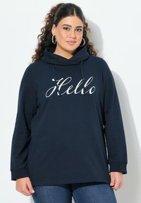 Felpa a maniche lunghe blu navy con collo a cappuccio e testo bianco "Hello". Tessuto morbido e vestibilità rilassata, abbinata a jeans in denim.