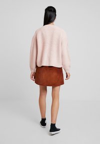 Hellrosa gestrickter Pullover mit kurzem Schnitt, kombiniert mit einem gebrannt-orangen Cordrock. Schwarze High-Top-Sneaker vervollständigen das Outfit.