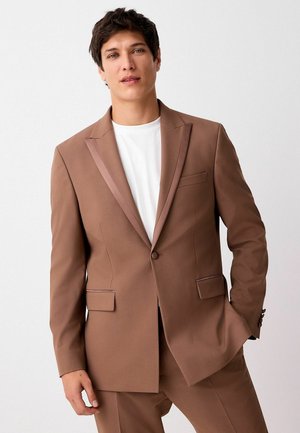 Brązowa marynarka z satynowym kołnierzem typu szal oraz dwoma przednimi kieszeniami. Gładka tekstura, dopasowany krój, zestawiona z białym t-shirtem pod spodem.