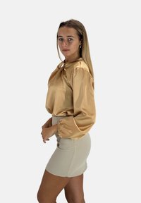 Top in raso marrone chiaro con vestibilità rilassata, scollo arrotondato e maniche a sbuffo; abbinato a una minigonna aderente beige chiaro.