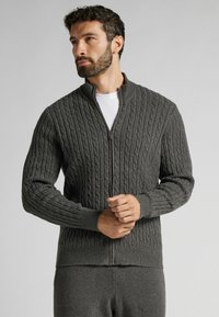 Šedý svetr se zipem, s texturou pleteného vzoru, žebrovanými manžetami a límcem. Vyroben z měkkého, teplého materiálu, s hladkým zipem.