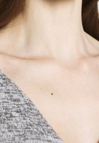 Top grigio in maglia con scollatura a V, che mette in mostra una trama del tessuto liscia e un sottile contrasto con il tono della pelle sul collo con una piccola macchia scura.