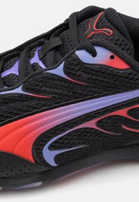 Zapato deportivo negro con parte superior de malla, acentos rojos y morados, diseño de olas dinámicas y suela texturizada. Cuenta con cordones y cuello acolchado.