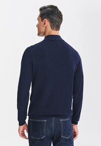 Granatowy dzianinowy sweter z wysokim kołnierzem, ściągaczami na mankietach i w pasie. Miękka tekstura, dopasowany krój i bezszwowe wykończenie na ramionach.