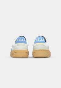 Baskets en cuir avec un design blanc et bleu clair, dotées d'une semelle en caoutchouc beige et d'un logo VEJA sur le talon. Texture douce et forme arrondie.