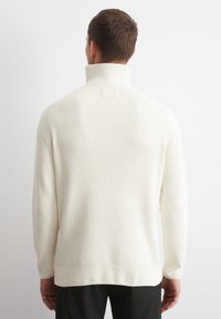 Cremefarbenes, geripptes Sweatshirt mit hohem Kragen, gestrickter Textur und langenÄrmeln. Der Saum ist leicht verlängert und sorgt für eine lässige Passform.