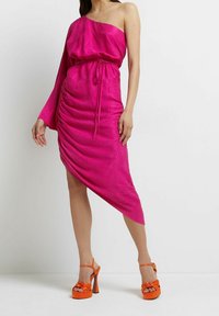 Fuchsiové šaty na jedno rameno s vypasovaným pasem, řasenou texturou a asymetrickým lemem. V kombinaci s jasně oranžovými platformovými podpatky s mašlemi.